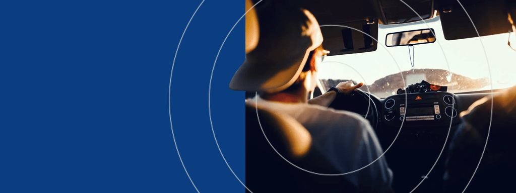 A person wearing a cap drives a car with sunlight streaming through the windshield, viewed from the back seat, perhaps navigating through visitor parking with Wayleadr's precise parking management system.