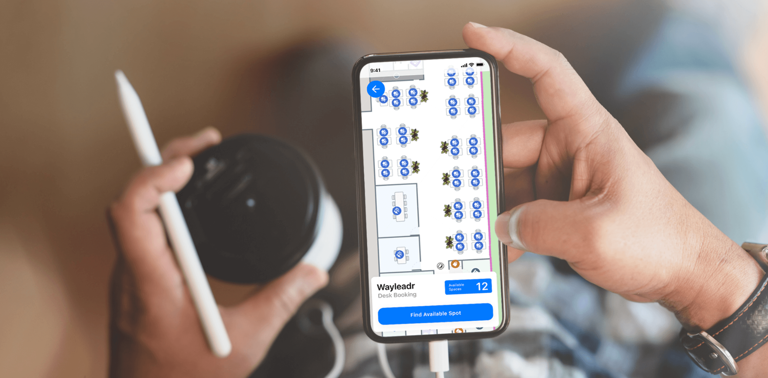 Person holding a smartphone displaying a desk booking app and holding a cup with a lid and a pen in the other hand.
