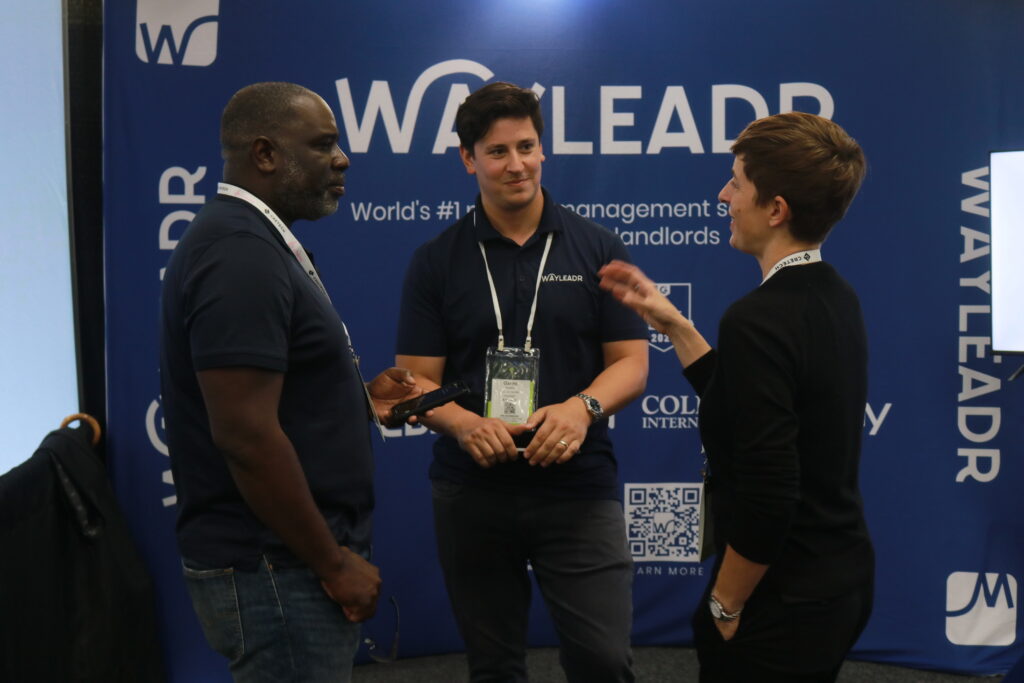 Three people standing and talking in front of a blue backdrop with "Wayleadr" branding at an event.