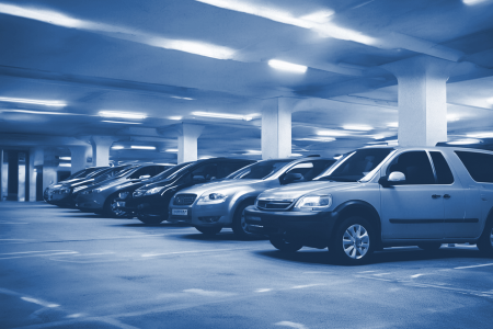 A row of parked cars in a dimly lit underground parking garage with concrete pillars and overhead lighting showcases the efficiency of professional parking management.