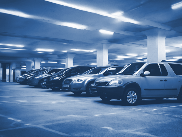 A row of parked cars in a dimly lit underground parking garage with concrete pillars and overhead lighting showcases the efficiency of professional parking management.